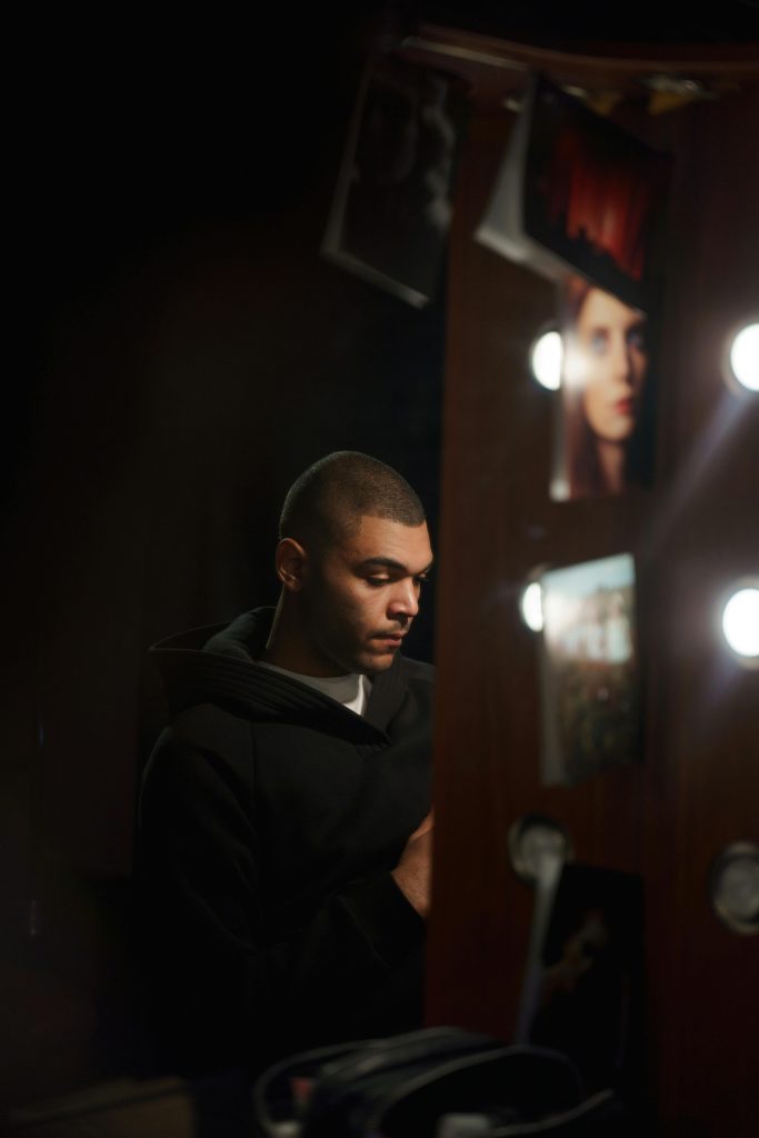 A thoughtful performer sits in front of a lighted mirror, capturing the essence of theater.